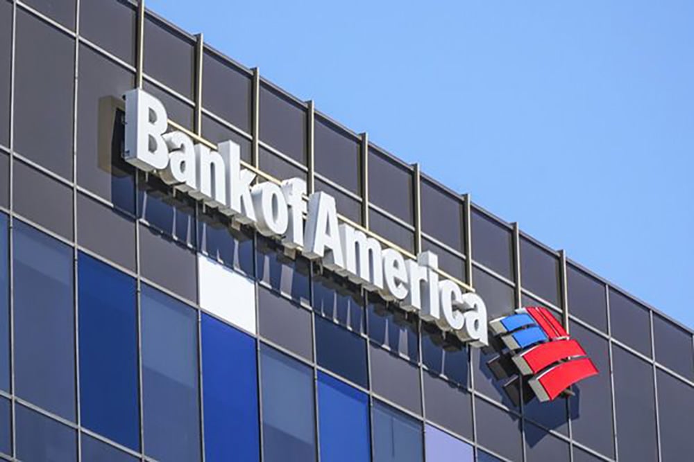 The Bank of America logo and name are displayed on the exterior of a modern glass building against a clear blue sky.