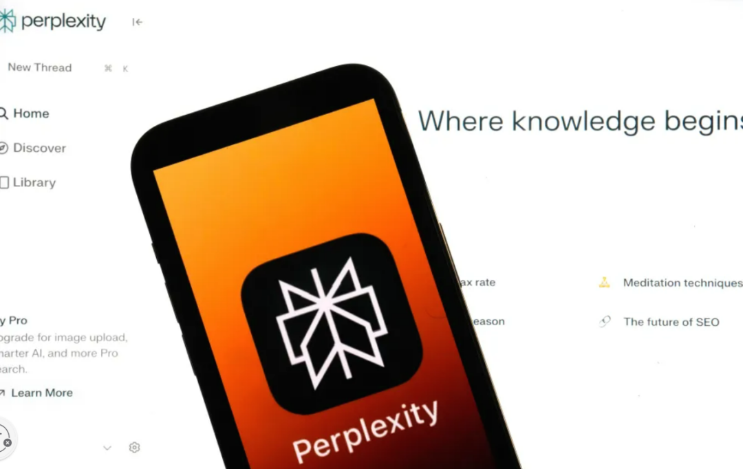 A smartphone displays the Perplexity app logo, featuring a white geometric star on a black background, in front of a blurred Perplexity website that reads "Where knowledge begi...".