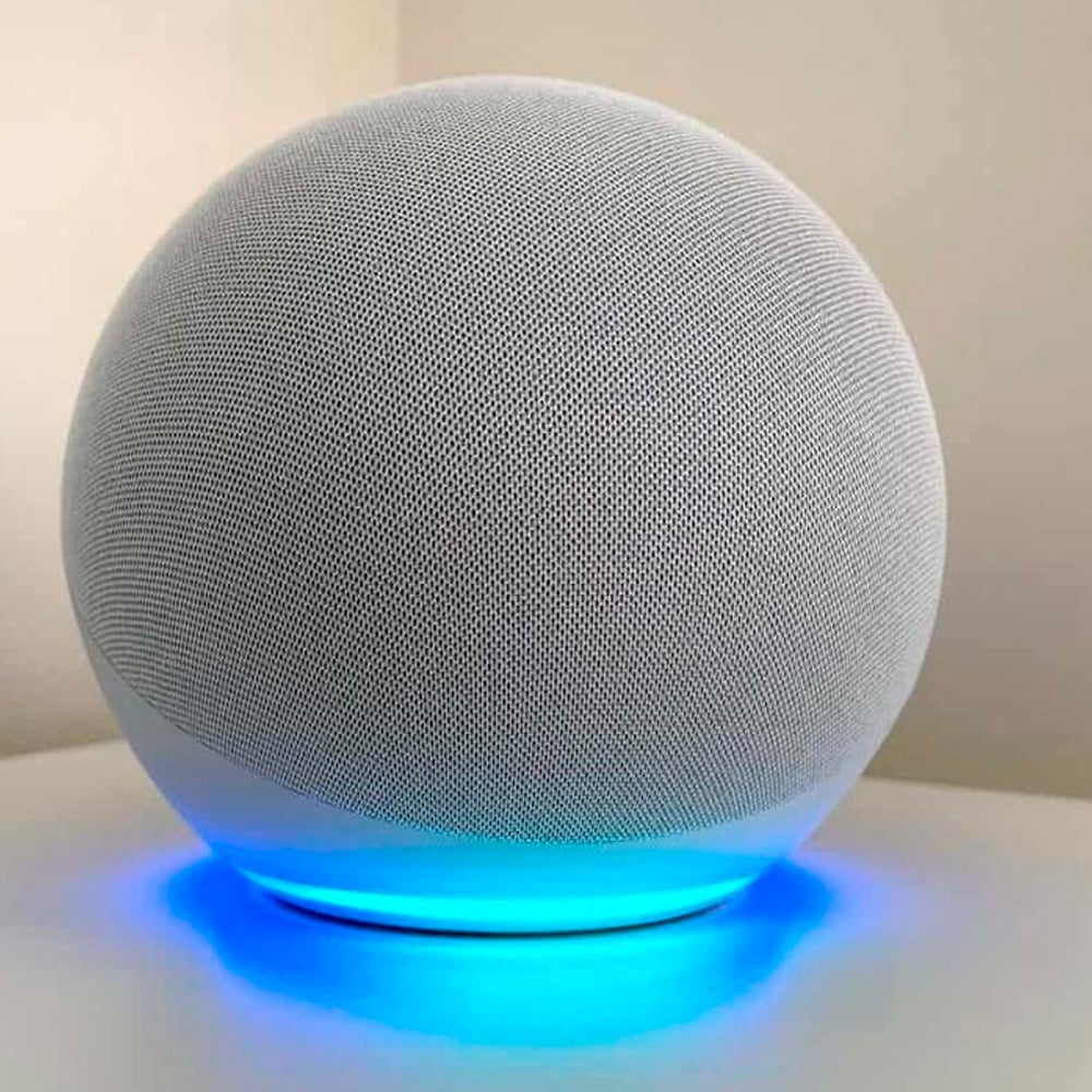 A spherical smart speaker with a mesh exterior sits on a white surface, glowing with a blue light at its base against a neutral background.