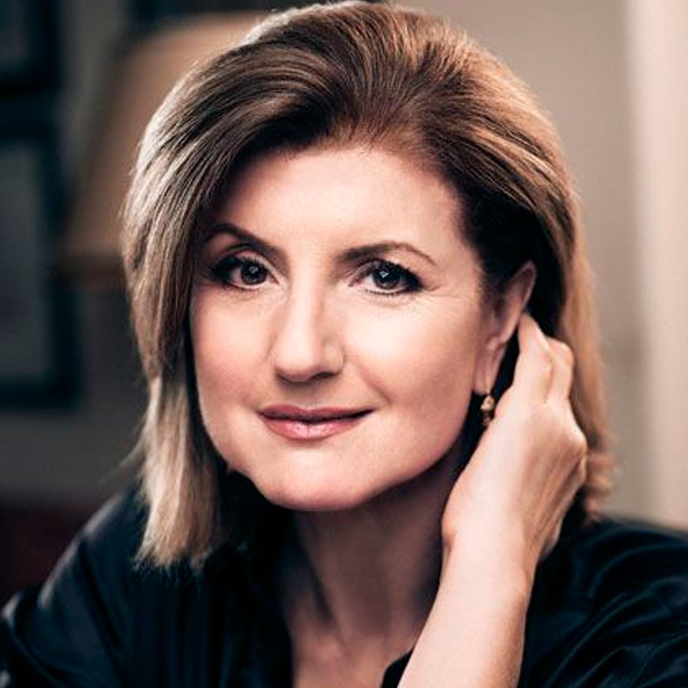 A woman with shoulder-length light brown hair and fair skin smiles gently, resting her head on her hand. She wears a dark top and small earrings, with a softly lit background.