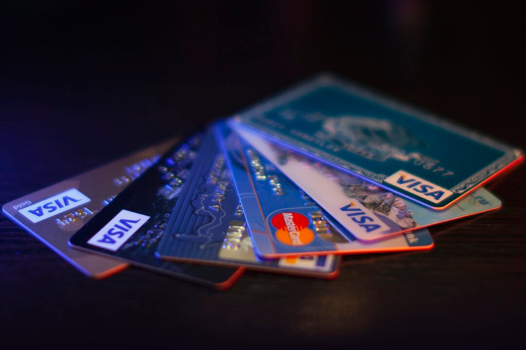A fanned-out stack of various credit cards, including Visa, Mastercard, and American Express, displayed on a dark surface under low lighting.