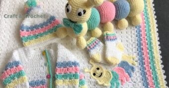 Crocheted baby items in white, pastel pink, blue, yellow, and green include a cardigan, hat with pom-pom, socks, a striped blanket, a large caterpillar toy, and a small caterpillar applique.