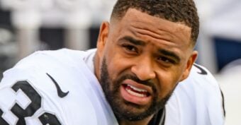 A football player in a white uniform with the number 23 is looking to the side with a focused expression. He has short hair, a trimmed beard, and is on the field during a game.