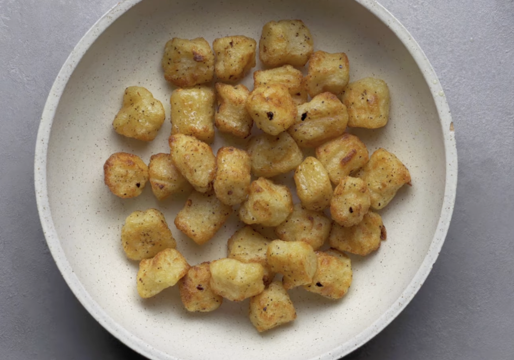A bowl of golden-brown pan-seared gnocchi seasoned with black pepper.