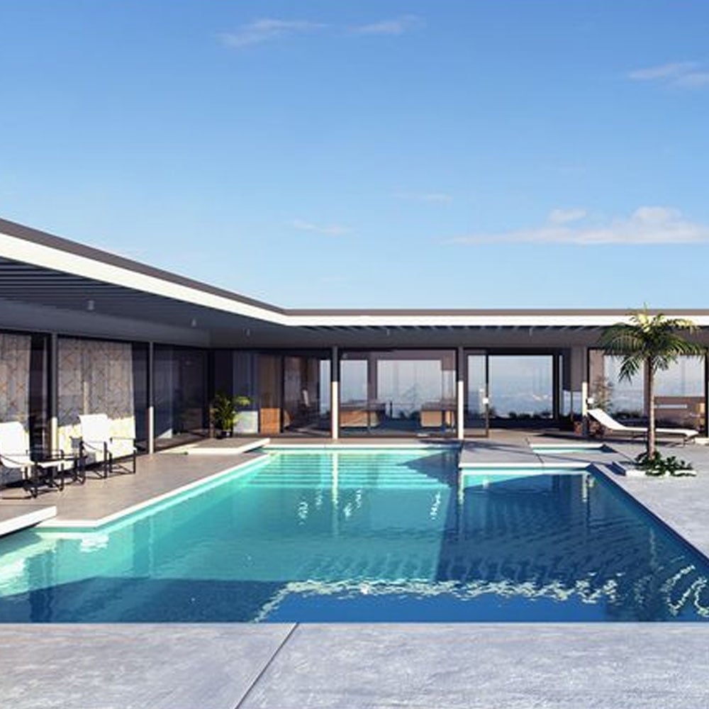 Modern house with large windows and a flat roof surrounds a rectangular outdoor swimming pool; poolside chairs and a small palm tree decorate the spacious, sunny patio under a clear blue sky.