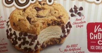 A close-up of an ice cream sandwich with chocolate chip cookies and vanilla ice cream, topped with chocolate chips. The packaging highlights &ldquo;Real Chocolate Chips&rdquo; and &ldquo;No RBST, No Artificial Colors.&rdquo;