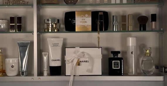 A shelf displaying luxury beauty products, including Chanel, Prada, and Gucci perfumes, skincare, and makeup items, all neatly arranged in glass shelves with some gift-wrapped boxes.