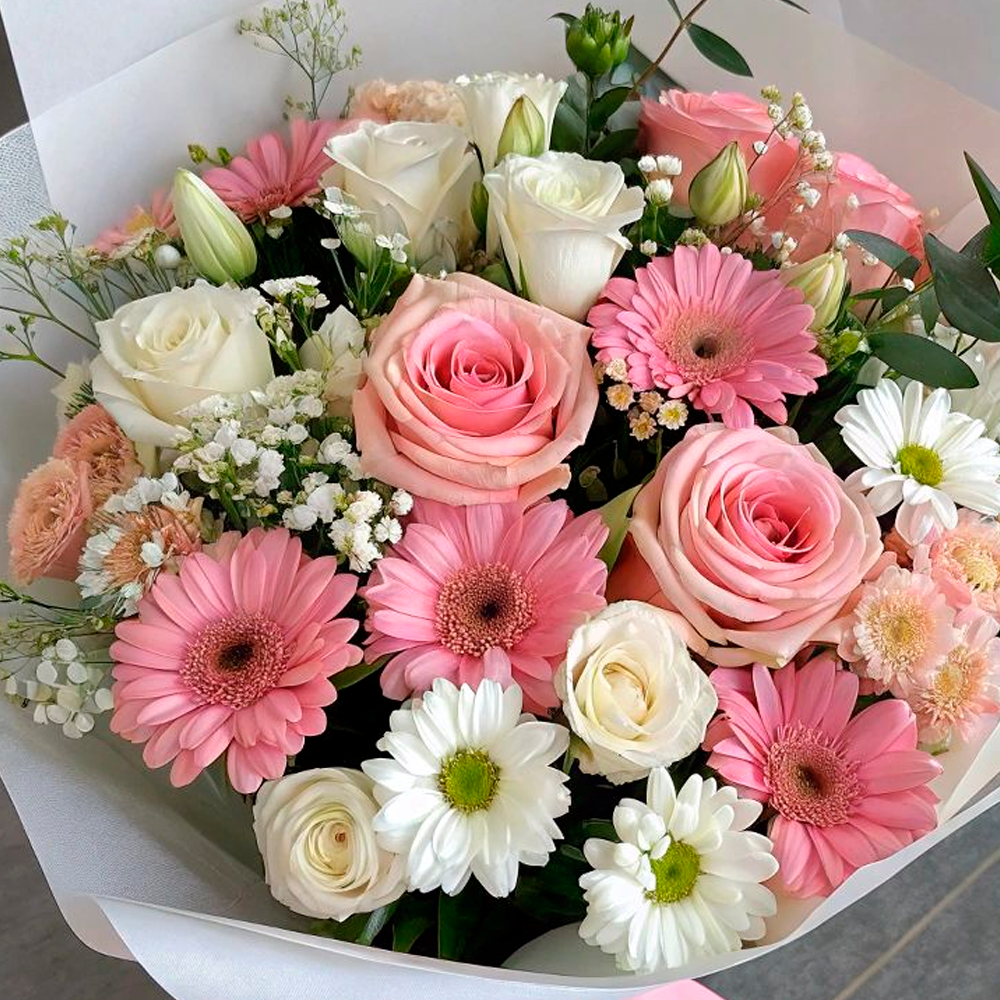 A bouquet of pink and white flowers, including roses, gerberas, daisies, and baby's breath, arranged with green foliage and wrapped in white paper.