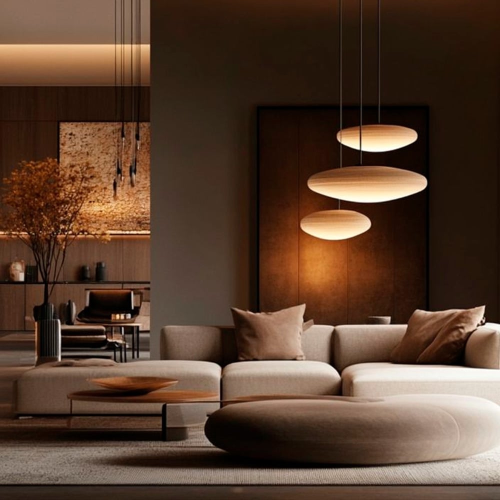 Modern living room with beige sectional sofa, round ottoman, wooden coffee table, warm pendant lights, and minimalist decor in earthy tones. Art and plants add elegance to the sophisticated, softly lit interior.
