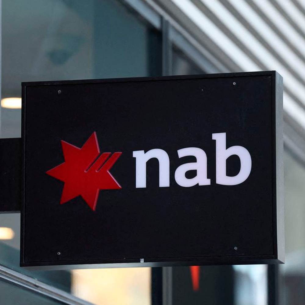 A sign displaying the NAB logo, featuring a red six-pointed star next to the lowercase white letters "nab" on a black background, attached to the exterior of a modern building.