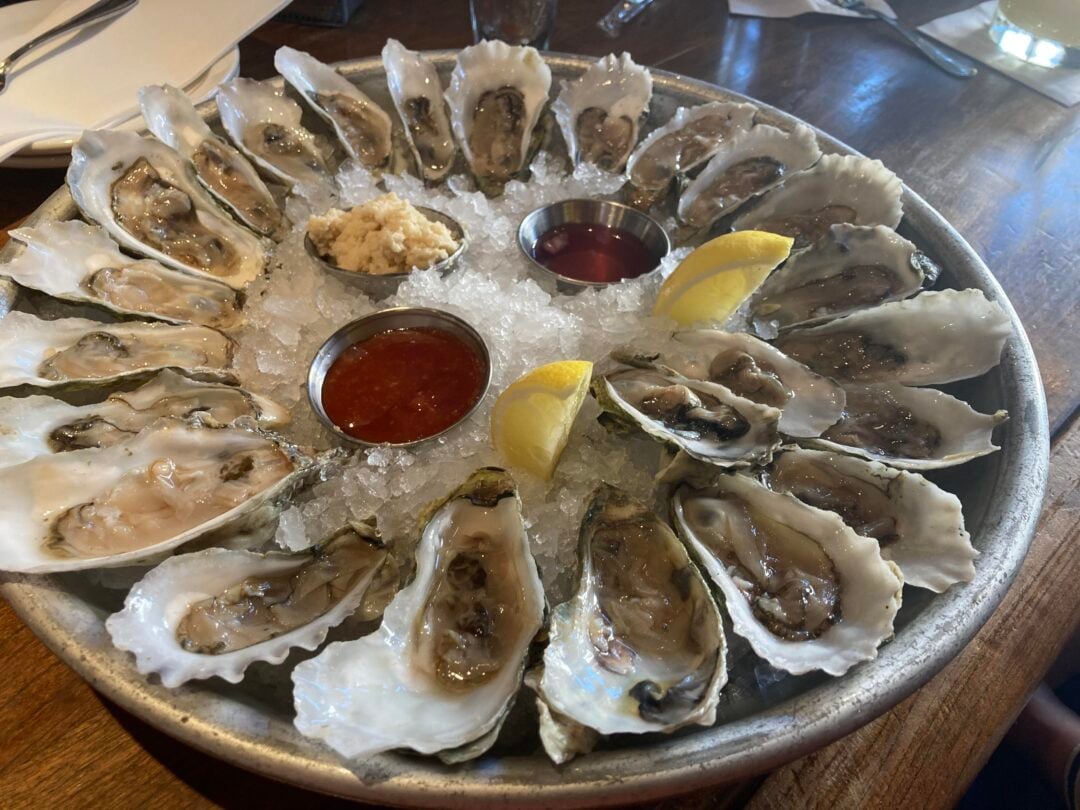 A hand holds a large, unusually shaped Dorito next to an open red bag of Doritos Nacho Cheese flavor. The scene is inside a car, with a steering wheel and leg in the background.