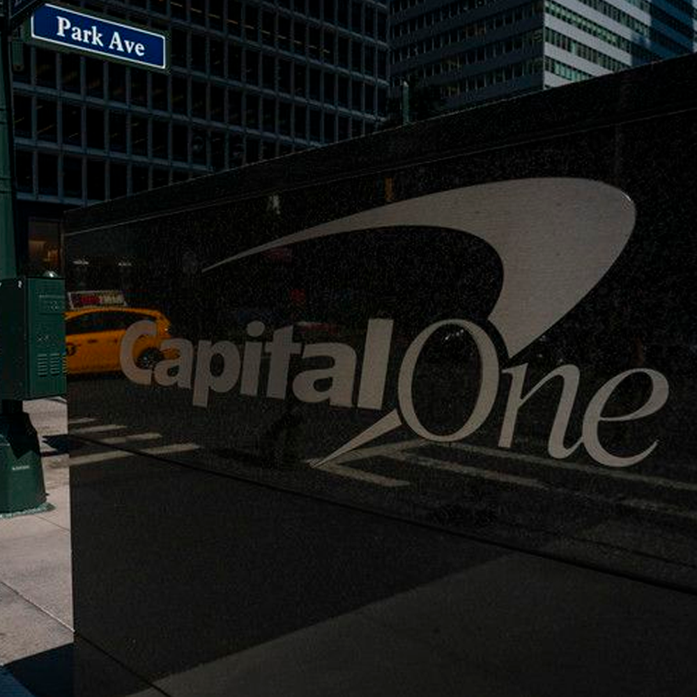 Capital One sign on a shiny black wall, reflecting a yellow taxi and city buildings, with a blue Park Ave street sign visible above.