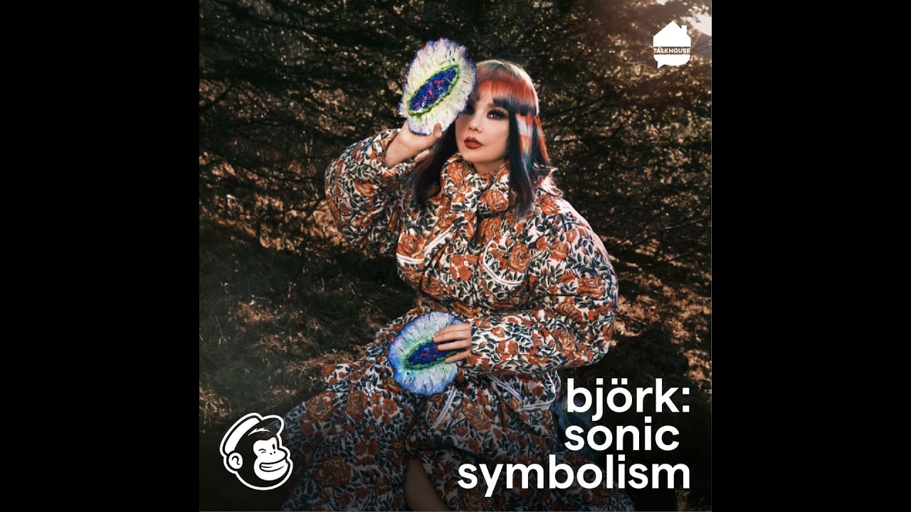A woman in a patterned dress sits outdoors, holding a colorful circular object to her face and another in her lap. Text reads "björk: sonic symbolism" with a monkey logo in the lower left and another logo at the top right.