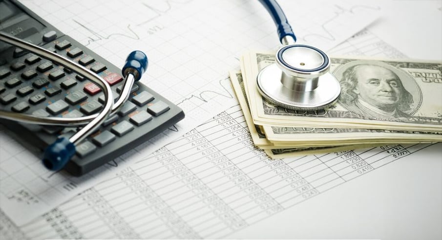 A stethoscope, calculator, and a stack of hundred-dollar bills rest on financial documents with charts, symbolizing the costs and financial aspects of healthcare.