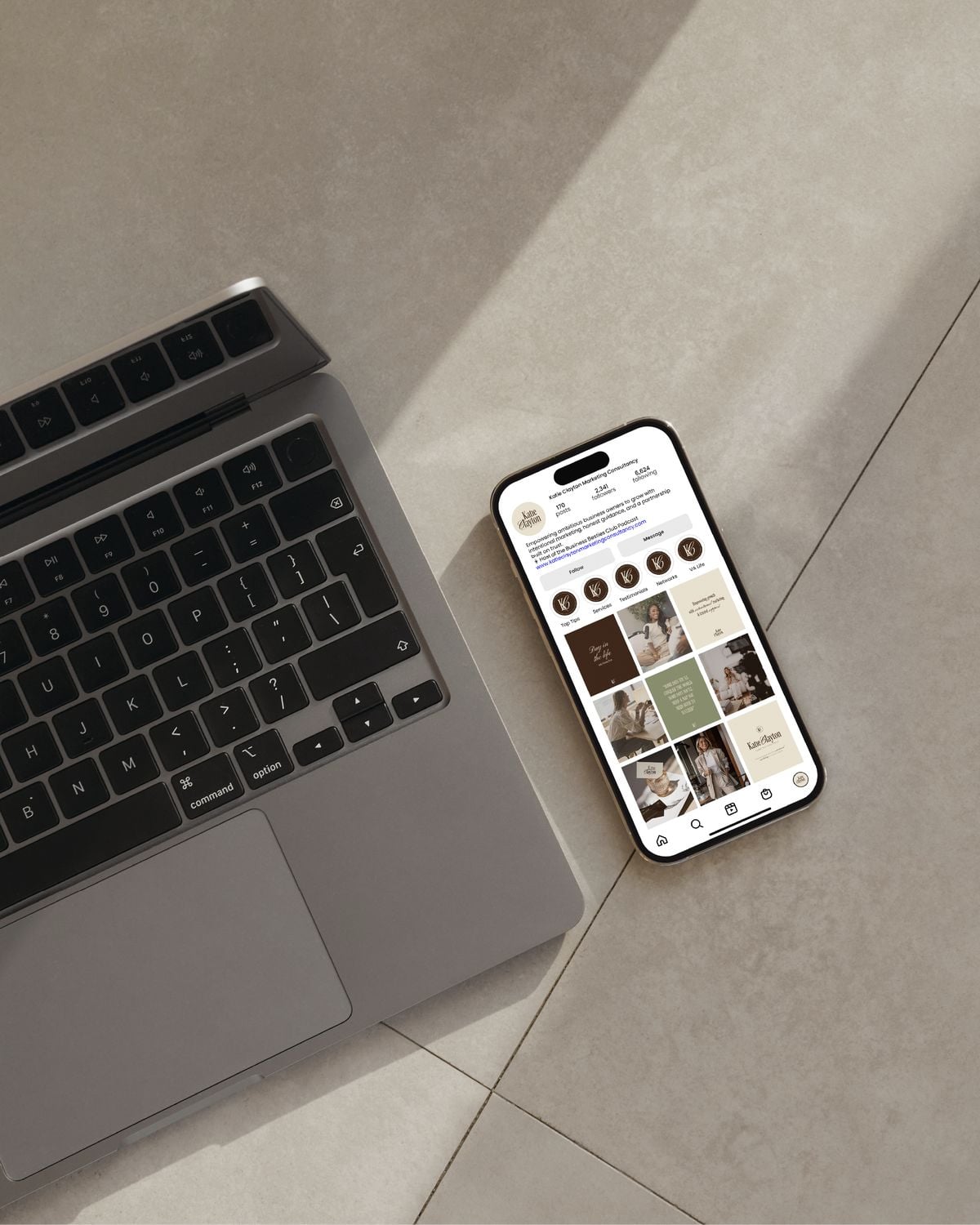 A laptop and a smartphone displaying an Instagram profile with a neutral-colored aesthetic are placed on a light-colored tiled floor, with sunlight streaming across the surface.