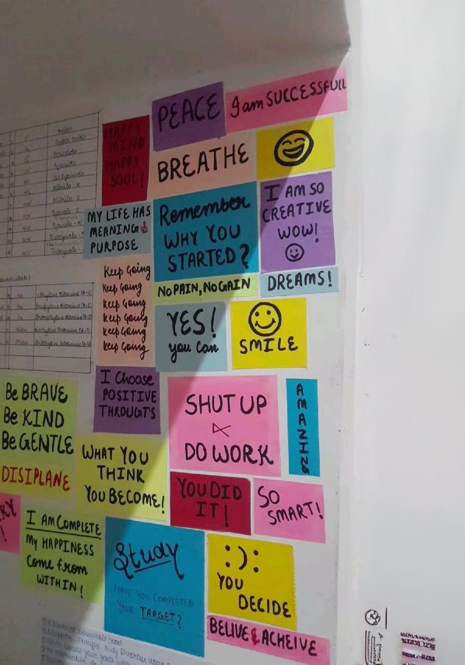 A wall covered with colorful sticky notes displaying motivational quotes like “BREATHE,” “Yes! you can,” “SHUT UP & DO WORK,” and “DREAMS!” Some notes include smiley faces and doodles.