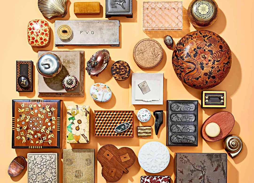 An assortment of decorative vintage boxes, cases, and containers of various shapes, sizes, patterns, and materials arranged neatly on a peach-colored surface.
