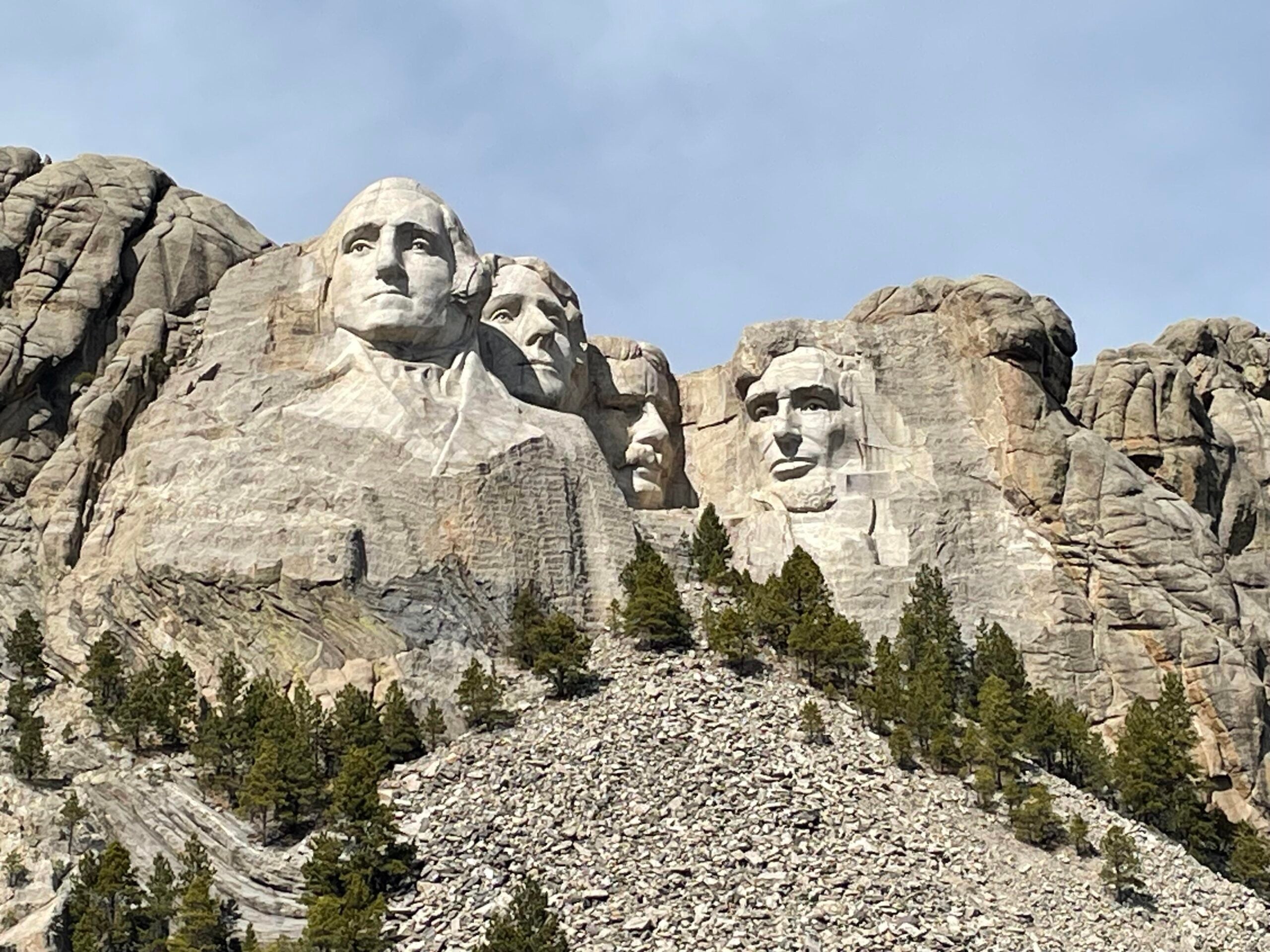 Mount Rushmore National Memorial with the carved faces of four U.S. presidents set in a granite mountain, surrounded by rocky terrain and pine trees under a partly cloudy sky.
