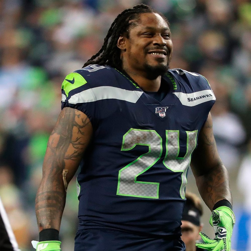 A smiling football player in a Seattle Seahawks uniform with the number 24 stands on the field, wearing navy blue and green gear.