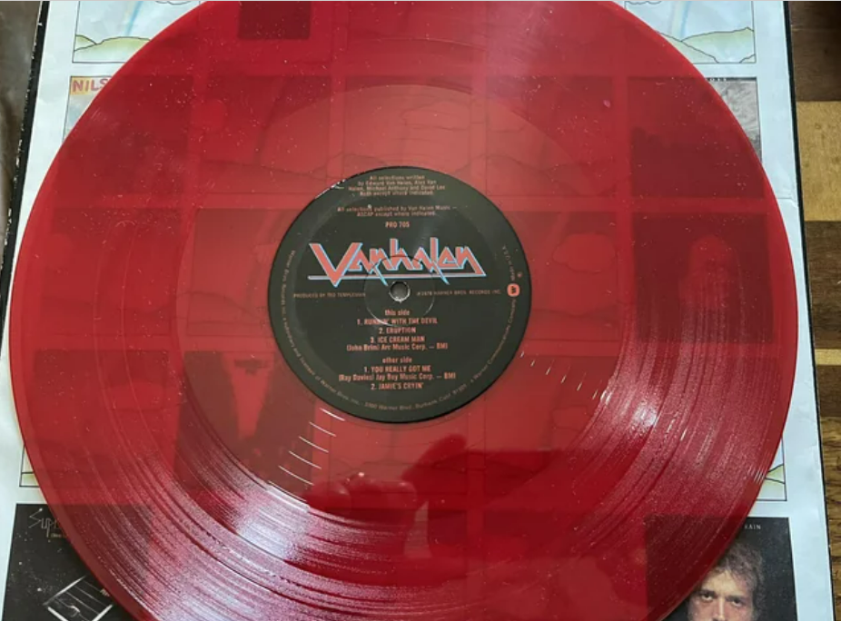 A translucent red vinyl record featuring the Van Halen logo and album details on the center label, resting on a patterned background.