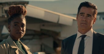 A woman with braided hair and a man in a suit stand outdoors in front of a blurred airplane, both looking slightly to the side with serious expressions.