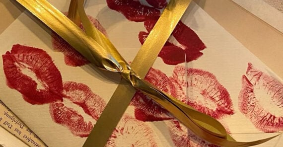 An envelope decorated with multiple red lipstick kiss marks, tied with a shiny gold ribbon.
