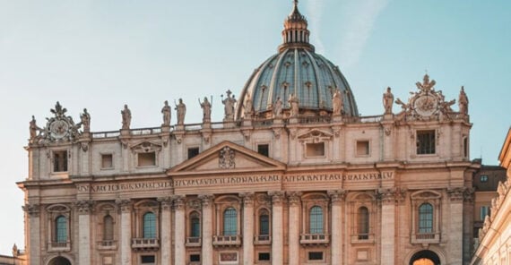 Ornate facade of St. Peter&rsquo;s Basilica in Vatican City at sunset, featuring classical columns, arched windows, and statues of saints on the roof against a clear sky.
