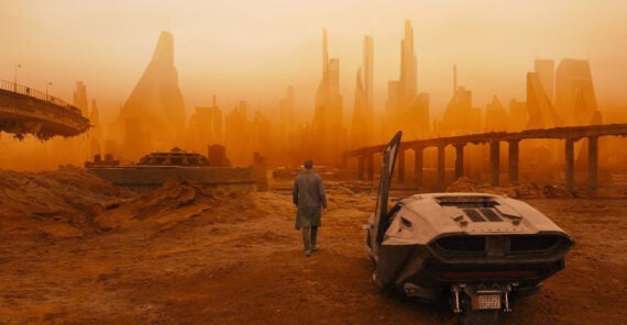 A person stands near a futuristic car, facing a hazy, orange-lit city with tall, modern skyscrapers and ruined overpasses in a desolate landscape.