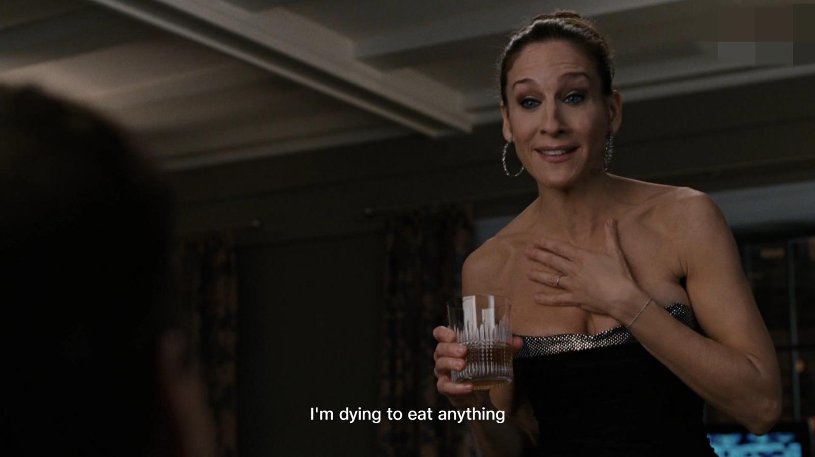 A woman in a strapless black dress holds a drink and touches her chest, speaking to someone off-screen. The subtitle reads, "I'm dying to eat anything.