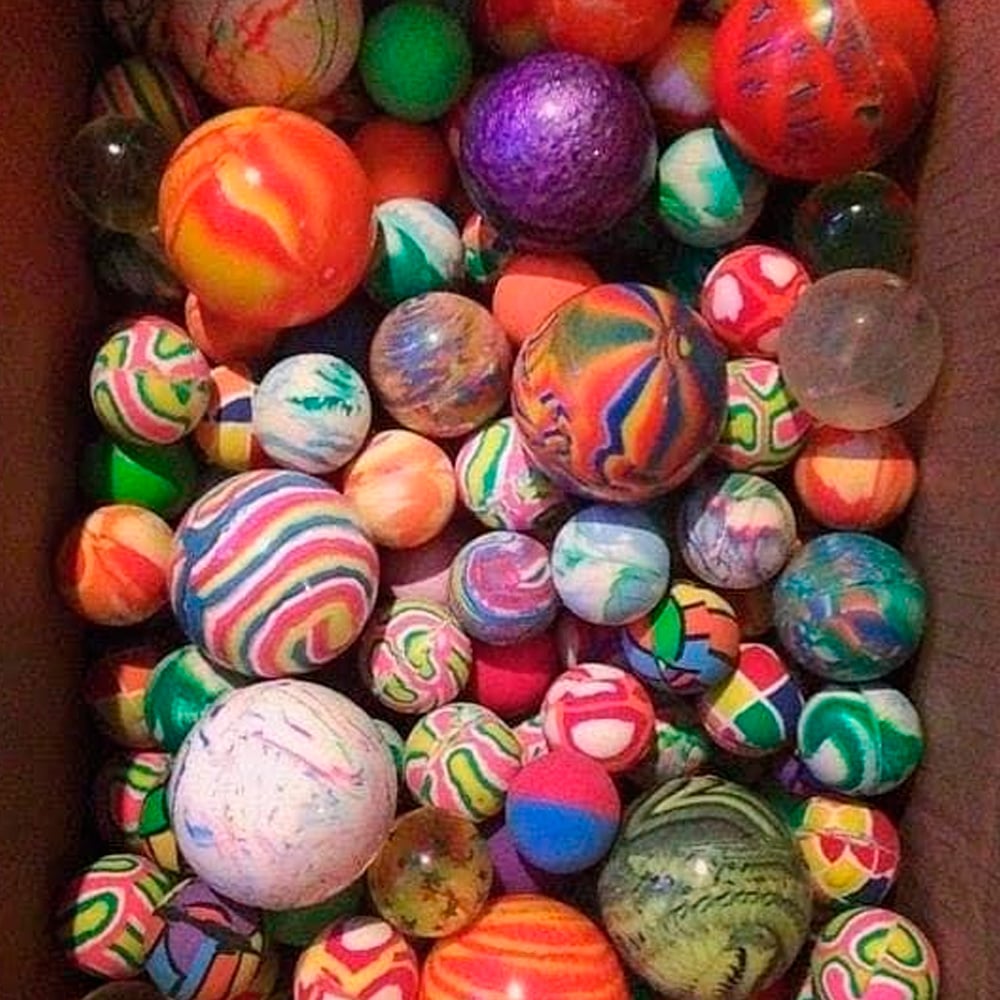 A box filled with dozens of colorful bouncy balls in various sizes and vibrant swirling patterns, including stripes, splatters, and marbled designs.