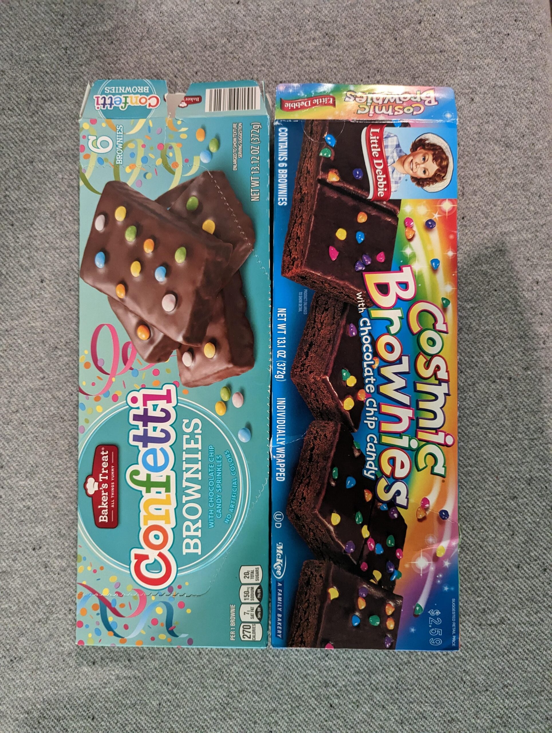 Two boxes of brownies on a gray surface: one is Betty Crocker Confetti Brownies with colorful candy pieces on a blue box, the other is Little Debbie Cosmic Brownies, also with colorful candy, on a rainbow box.