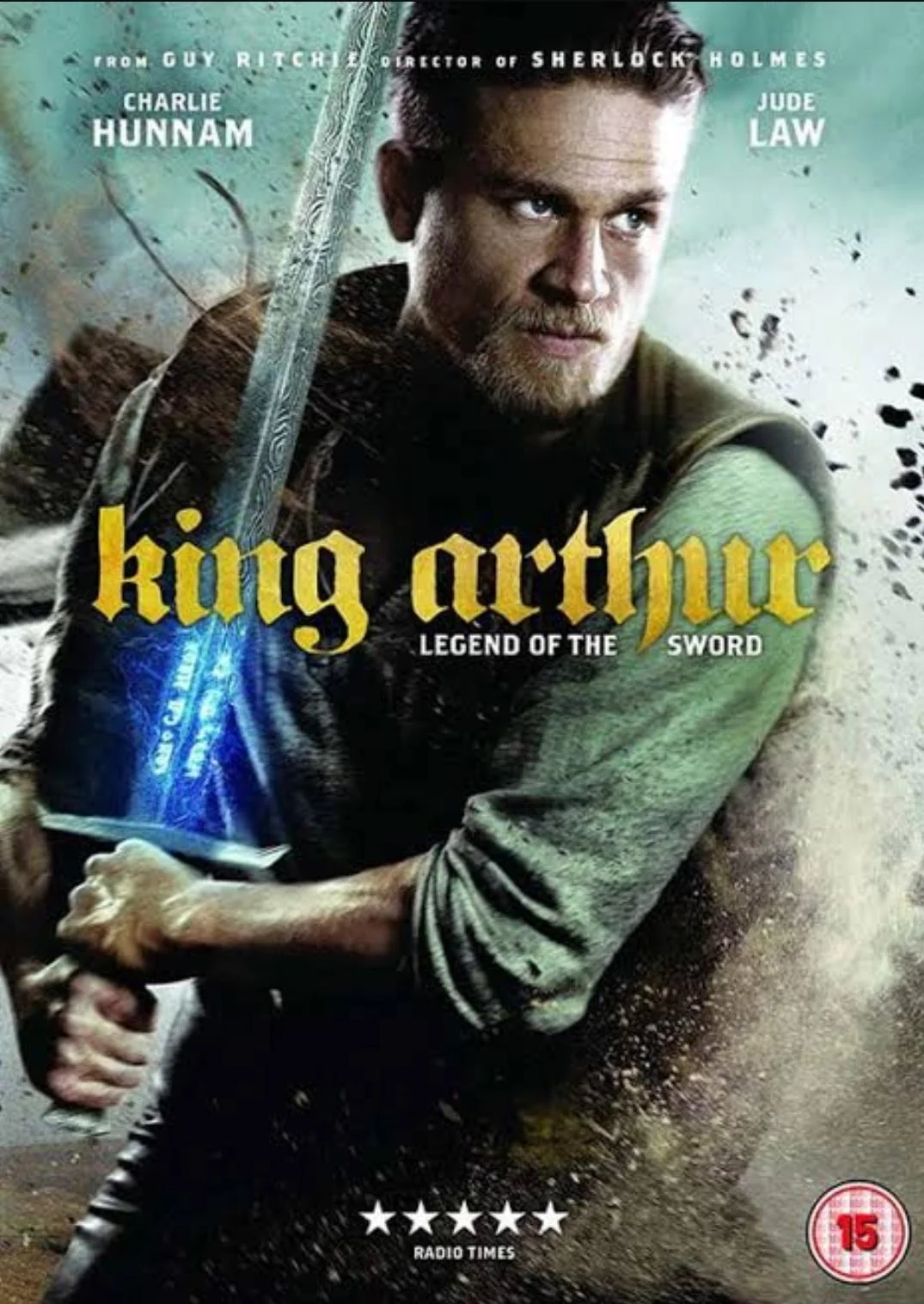 A man holds a glowing sword with both hands. The text reads "King Arthur: Legend of the Sword." Actor names Charlie Hunnam and Jude Law appear at the top. The background is dark and dramatic.