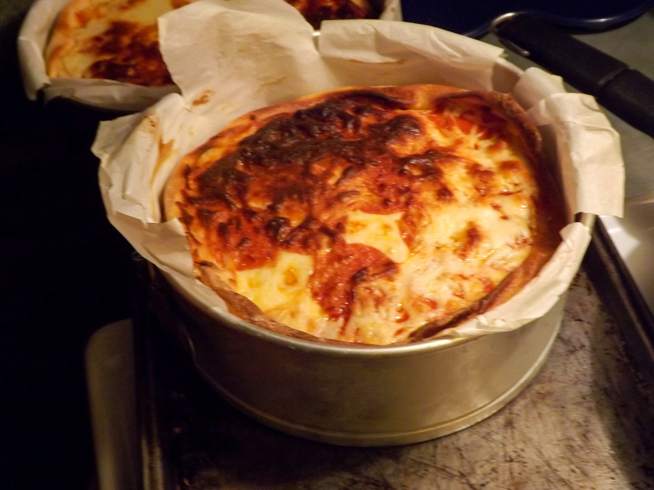 A freshly baked lasagna in a round springform pan lined with parchment paper, with a golden-brown, slightly crispy top layer, resting on a baking sheet.