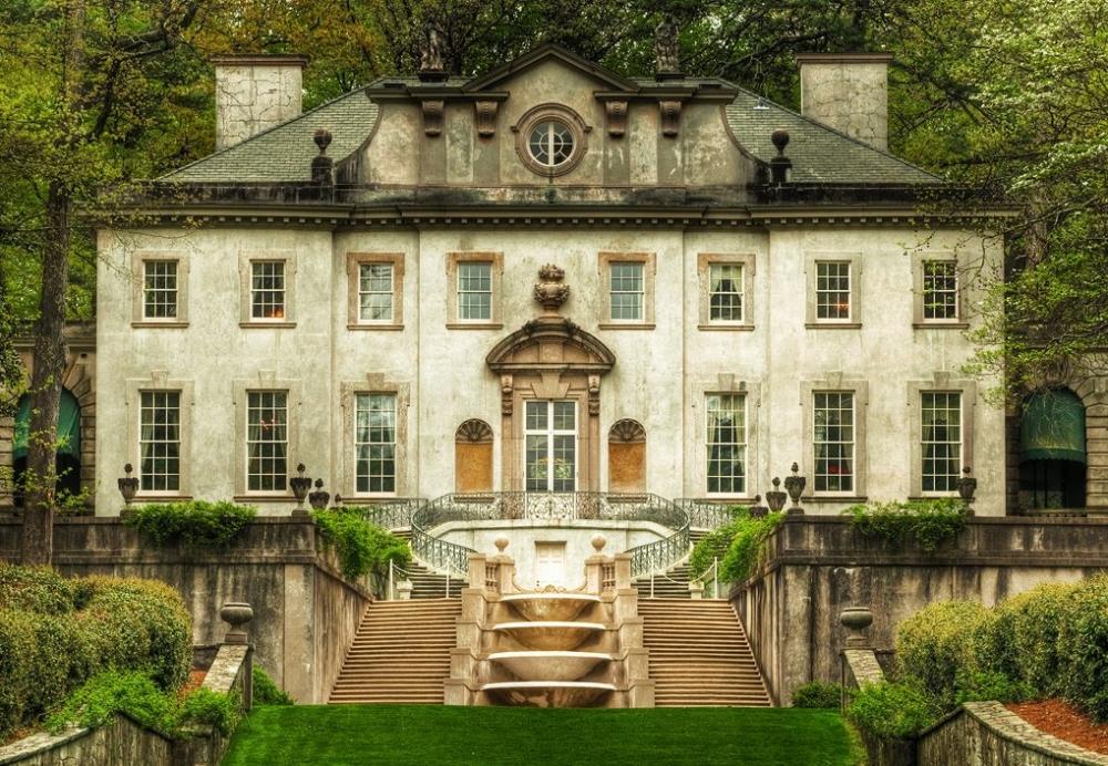 A grand, symmetrical mansion with tall windows, a central staircase, and ornate architectural details, surrounded by lush greenery and formal gardens.