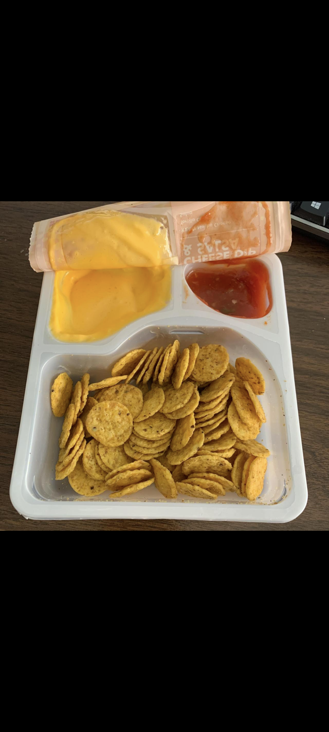 A tray with round crackers, a section of melted cheese dip, and a section of red dipping sauce, on a wooden surface. The cheese dip section has its lid partially peeled back.