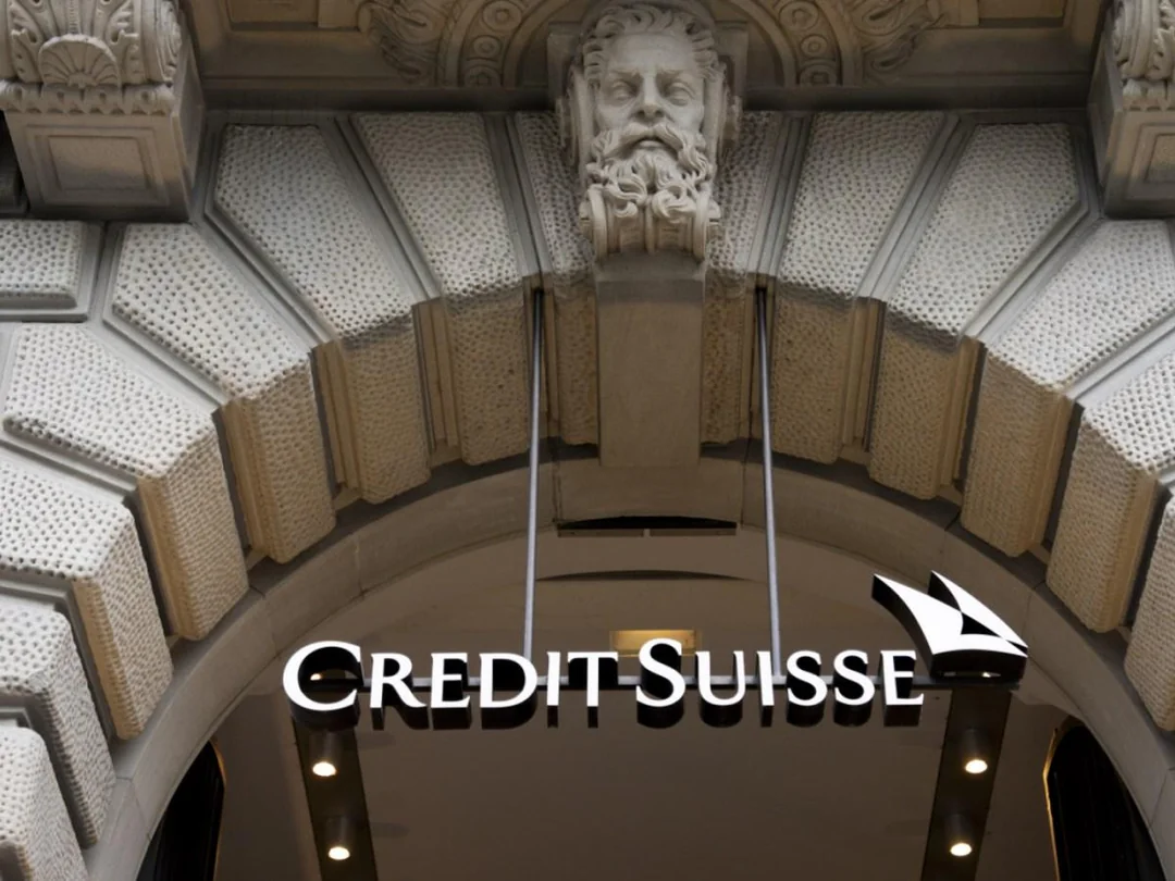 An arched stone entrance with a sculpted face above it and the illuminated Credit Suisse logo and emblem hanging below.