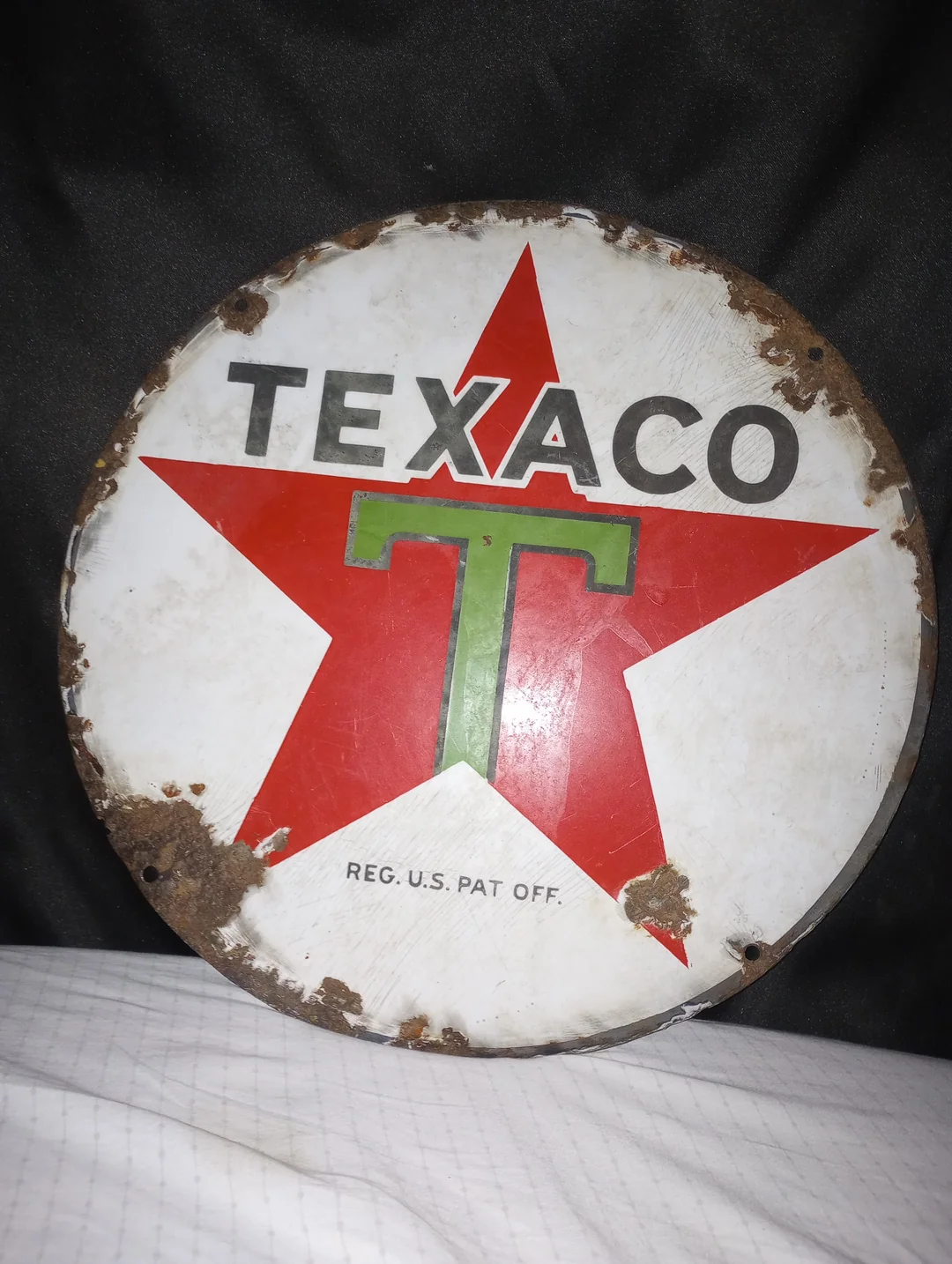 A vintage, rusted Texaco sign featuring a large red star, a green "T" in the center, and the word "TEXACO" above. The sign is set against a dark background.