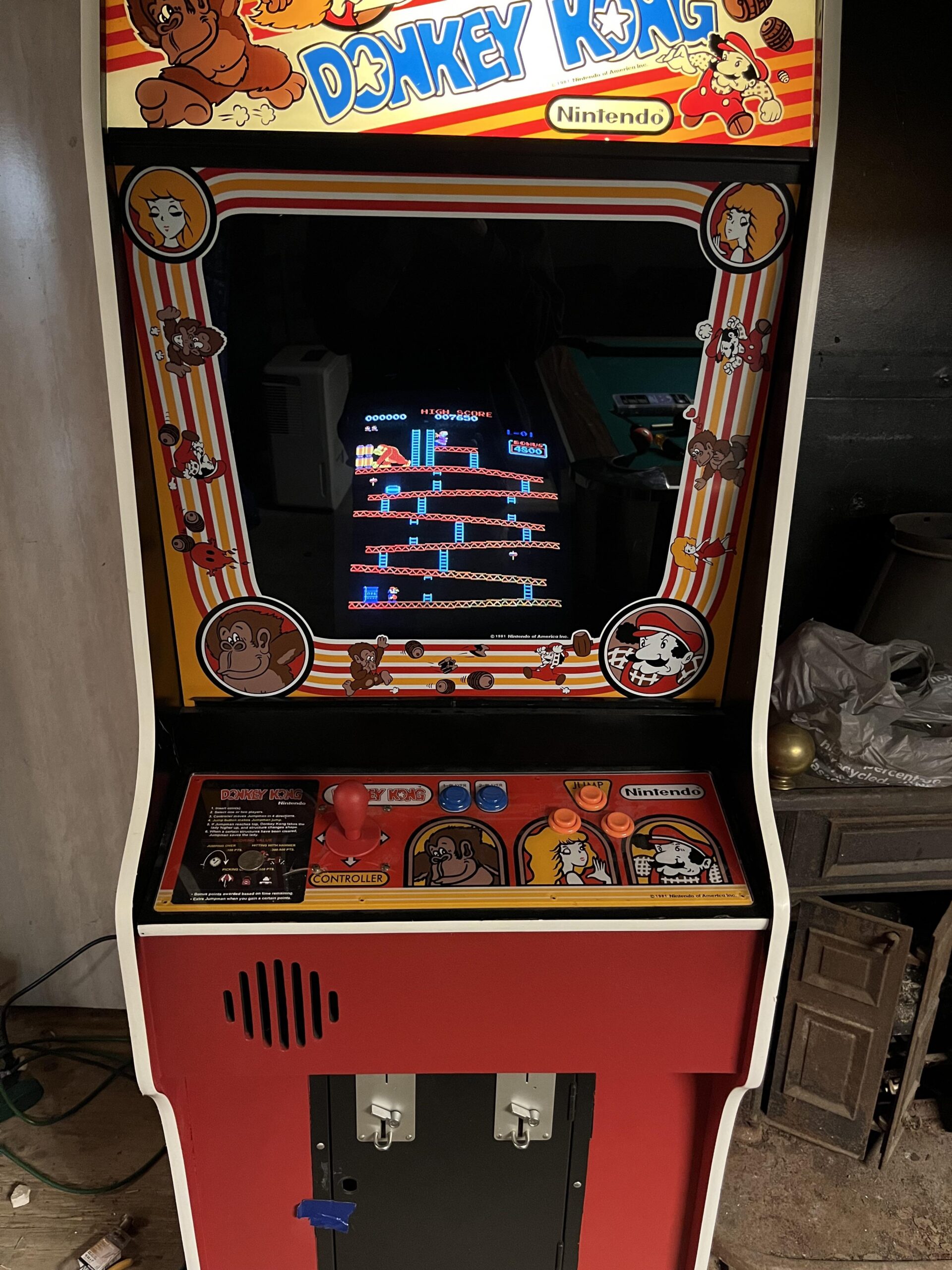 An upright Donkey Kong arcade machine with colorful artwork showing various characters. The game screen displays the classic platform levels. The control panel features a joystick and buttons.