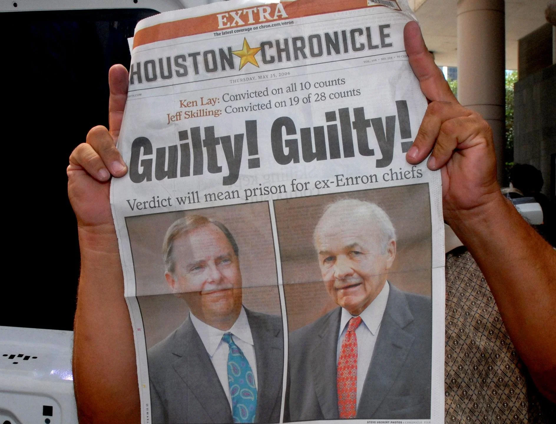A person holds up a copy of the Houston Chronicle newspaper with the headline “Guilty! Guilty!” and photos of Ken Lay and Jeff Skilling, announcing their convictions in the Enron scandal.