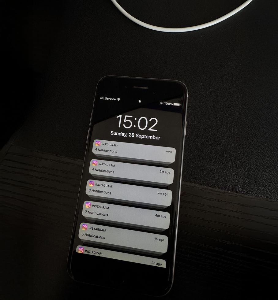 A smartphone on a dark table displays multiple Instagram notifications on its lock screen. The time is 15:02 on Sunday, 28 September, and the phone shows "No Service" in the signal area.
