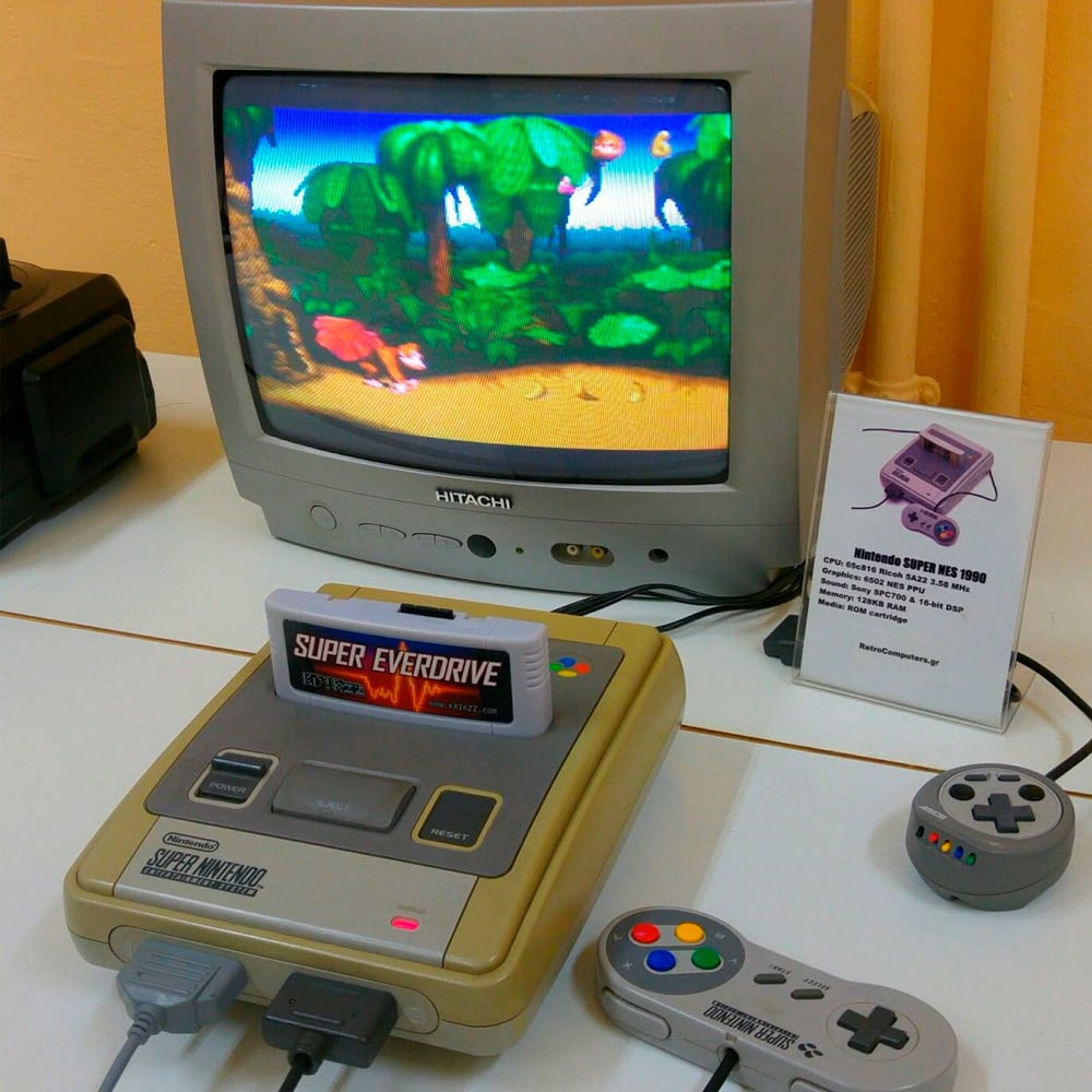 A retro gaming setup with a Super Nintendo console, two controllers, and a Super Everdrive cartridge, connected to a CRT TV displaying a colorful platform game. A small information card stands nearby.