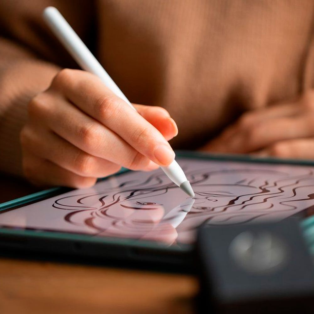 A person uses a stylus to draw a woman’s face on a digital tablet. The screen displays smooth, flowing lines, and the person’s hand is in focus, holding the pen above the tablet.