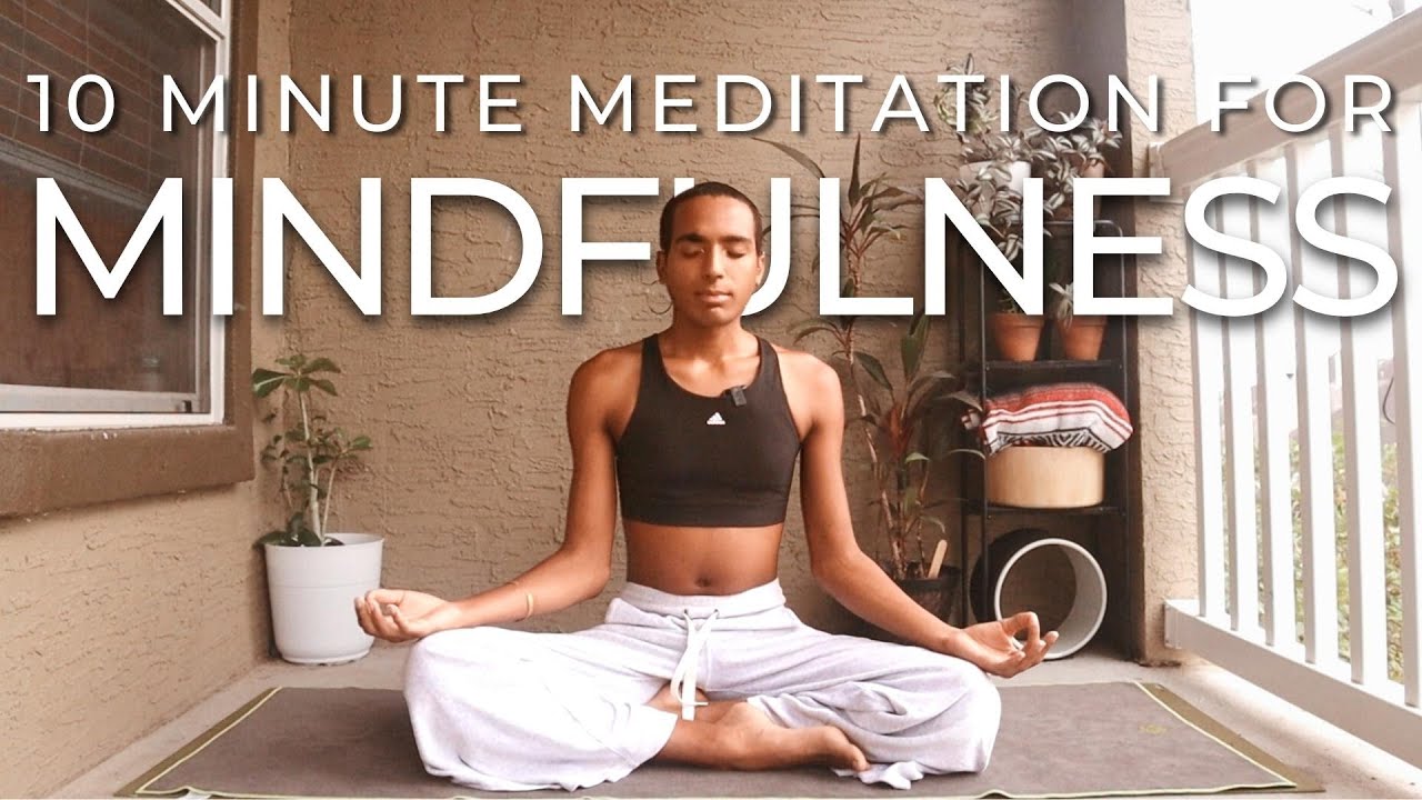 A person sits cross-legged on a mat in a meditation pose on a balcony. Text over the image reads, "10 Minute Meditation for Mindfulness." Potted plants and shelves are visible in the background.