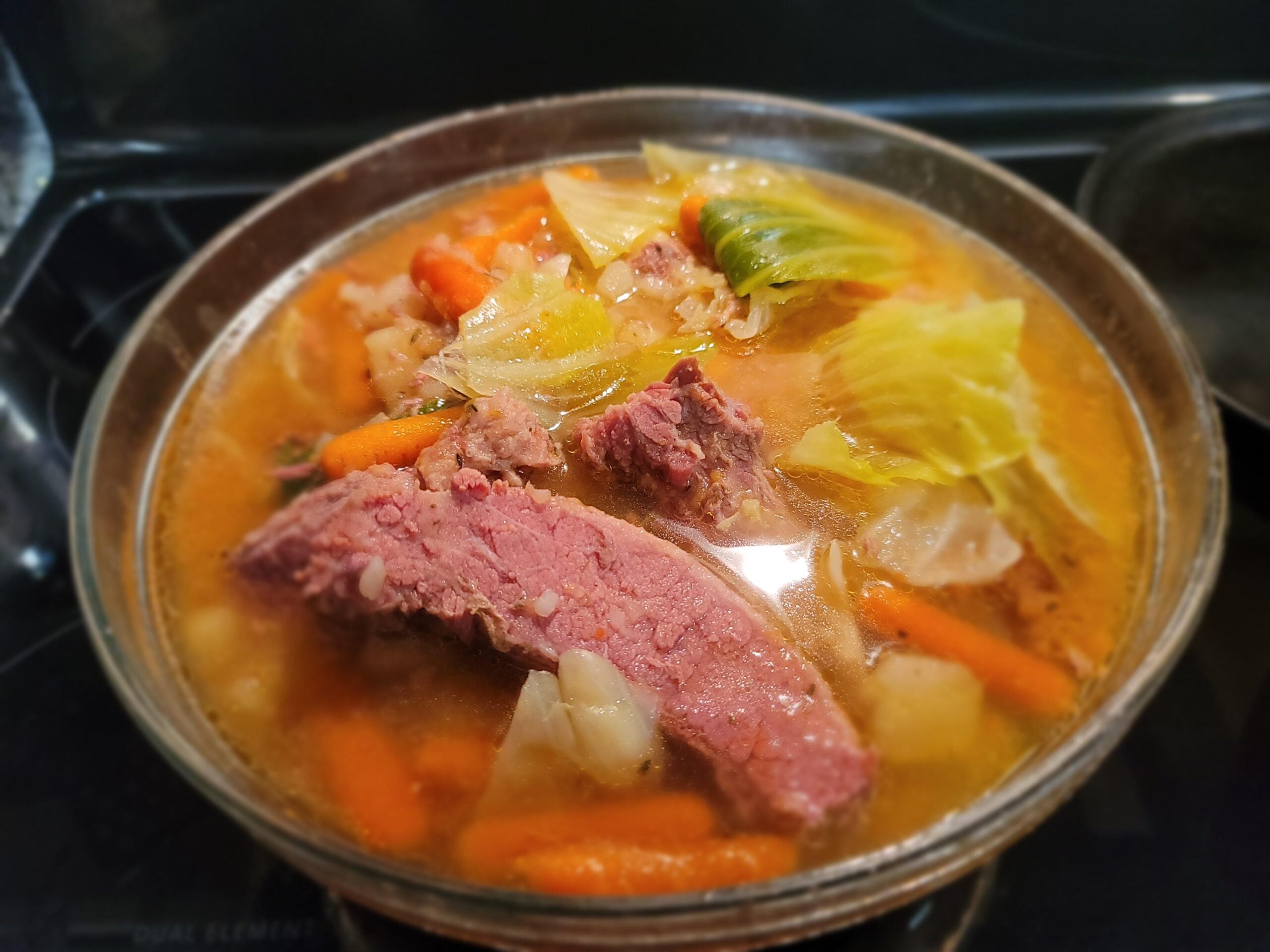 A pot of homemade corned beef and cabbage stew with sliced corned beef, chunks of cabbage, carrots, and potatoes in broth, simmering on a stovetop.