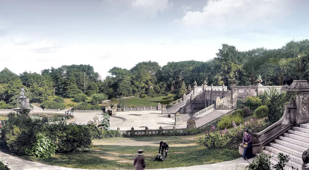 A landscaped park scene with wide stone stairs, ornate balustrades, statues, and people walking or sitting among lush green lawns, trees, and garden beds under a cloudy sky.
