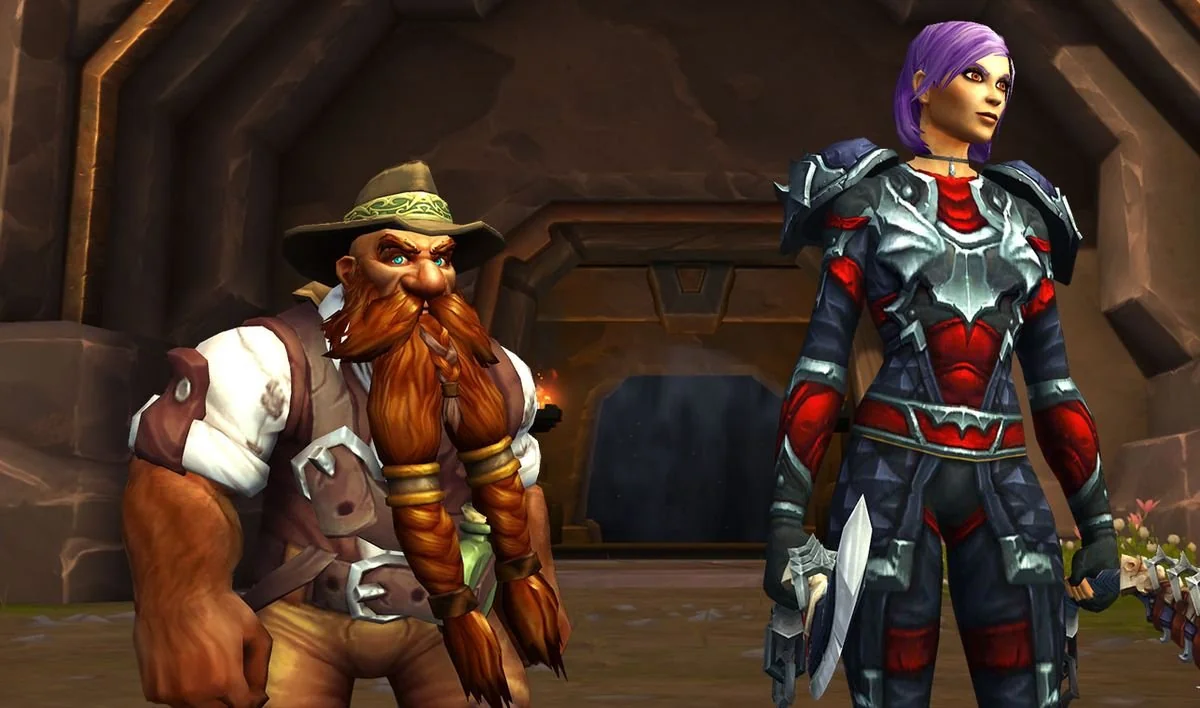 A dwarf with a long braided beard and explorer attire stands next to a woman in black and red armor holding a dagger, both in front of a stone doorway in a fantasy setting.