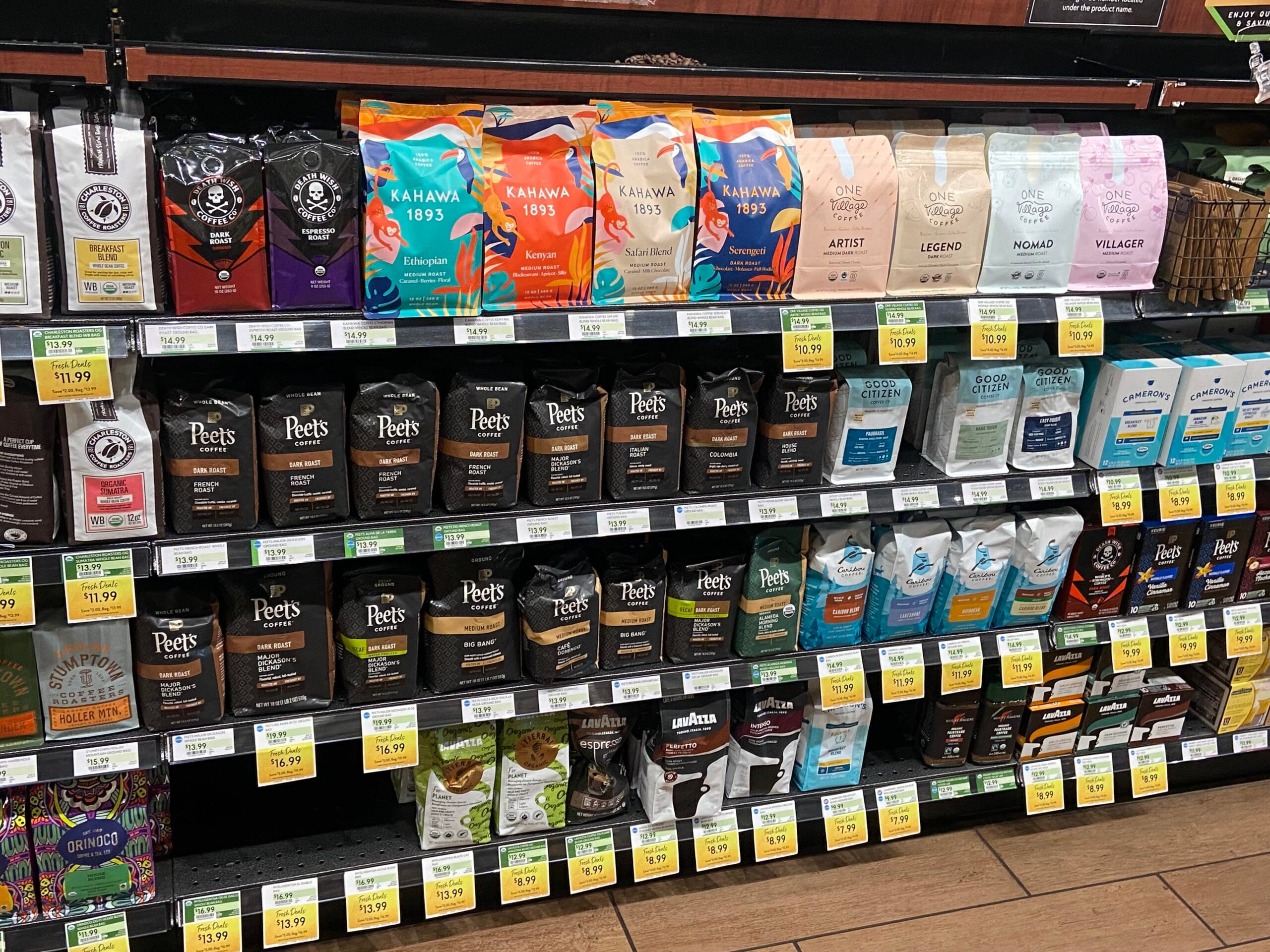 Rows of packaged coffee bags from brands like Peet's, Kahawa 1893, and others are neatly arranged on grocery store shelves, with price tags displayed below each product.