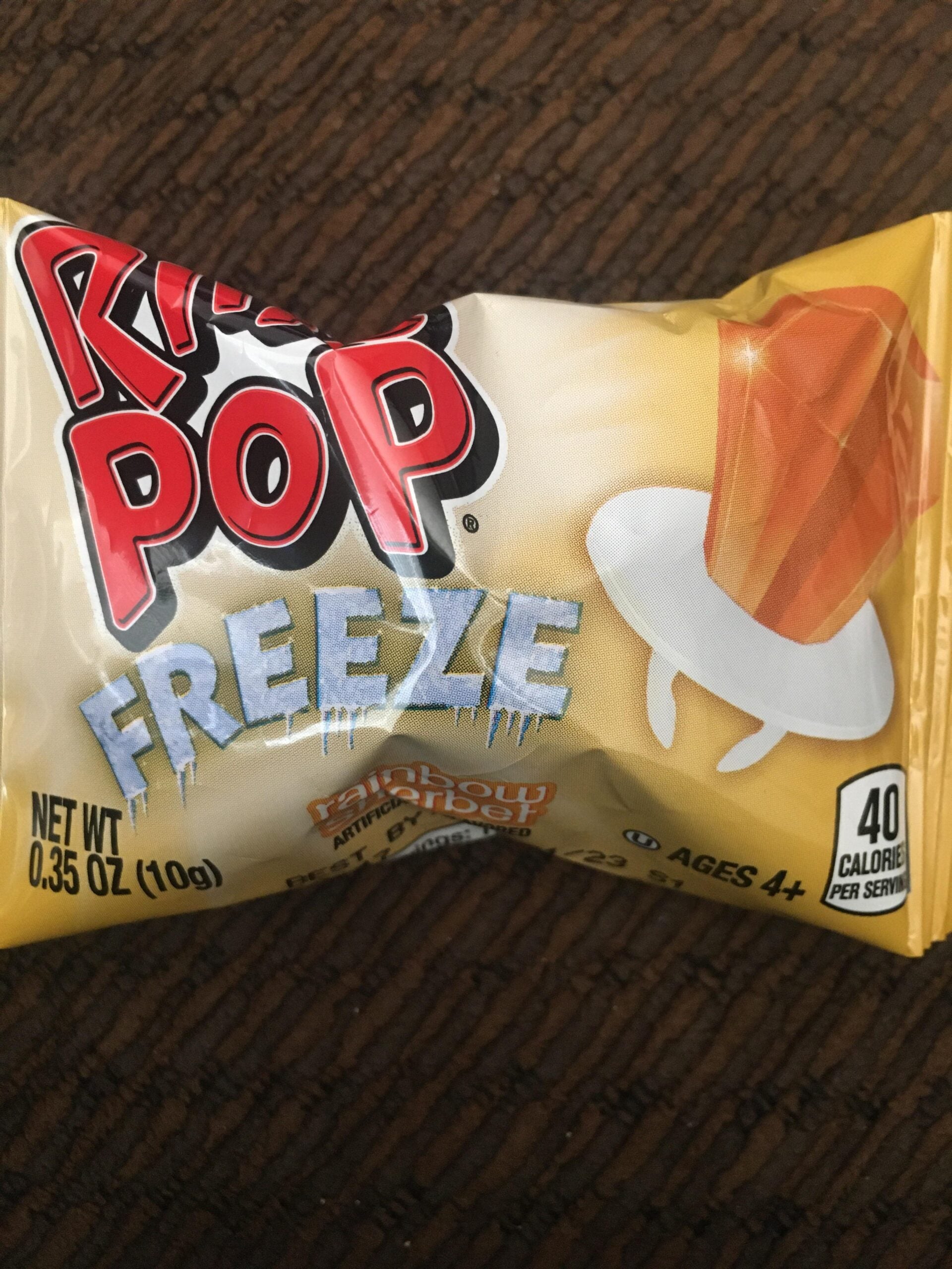 A close-up of a yellow package of Ring Pop Freeze candy, showing an illustration of an orange-colored Ring Pop and text indicating it has 40 calories per serving and is suitable for ages 4 and up.