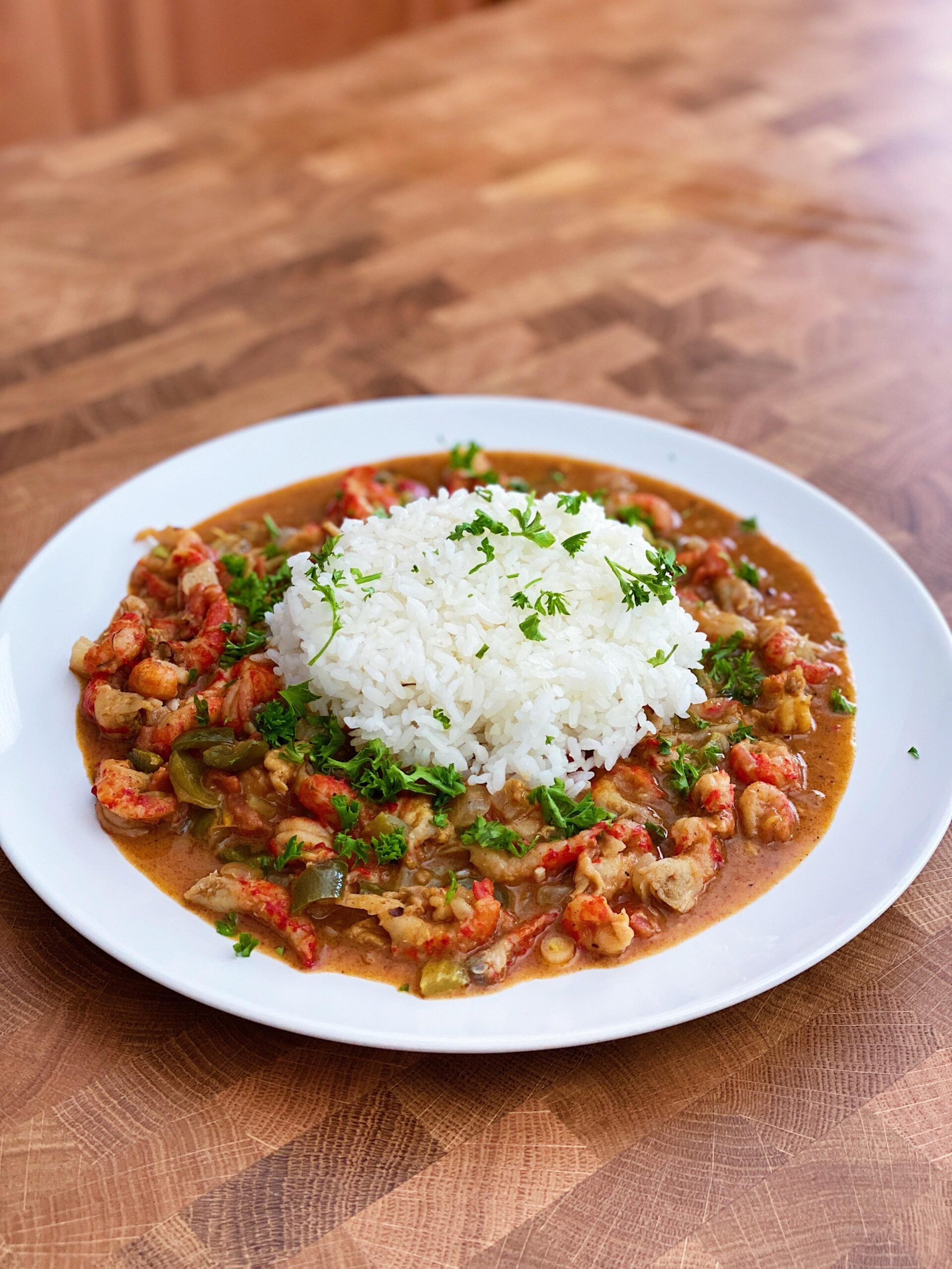 A white plate with a serving of white rice in the center, surrounded by a colorful stew with vegetables and herbs, garnished with fresh chopped parsley on a wooden table.