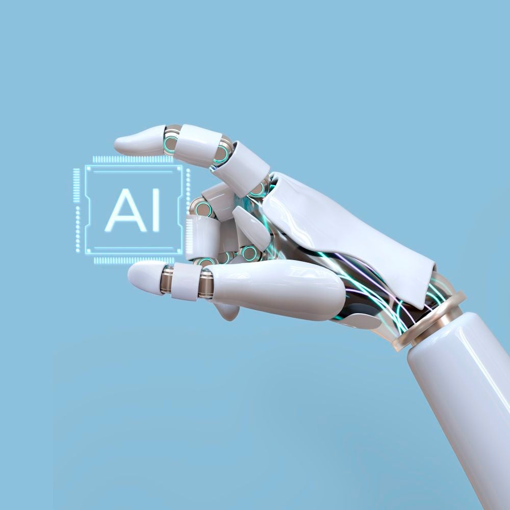 A robotic hand with white and metallic parts holds a glowing microchip labeled "AI" against a light blue background.